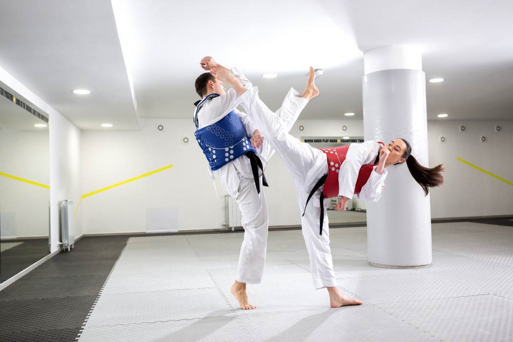 two taekwondo players exchanging high kicks during training